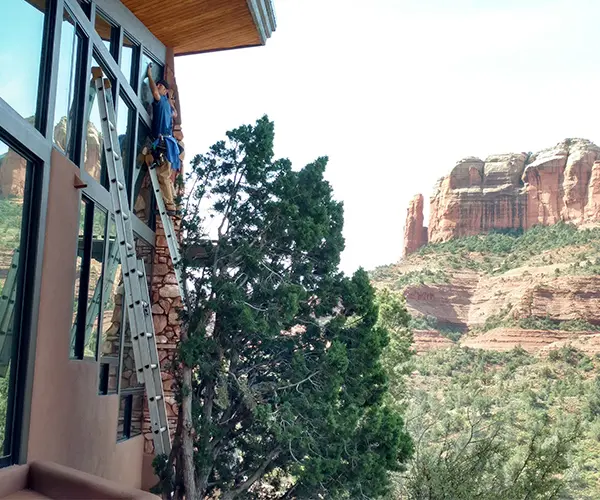 man up on a ladder cleaning windows with desert scenery in the background