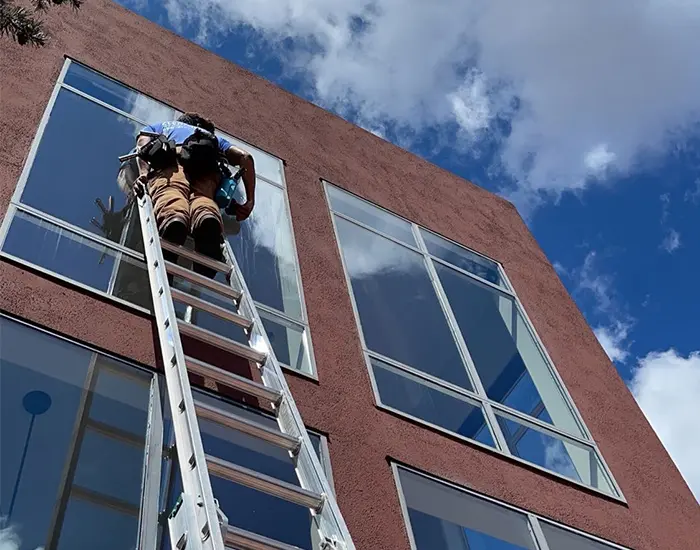 man up on a ladder against a building cleaning windows