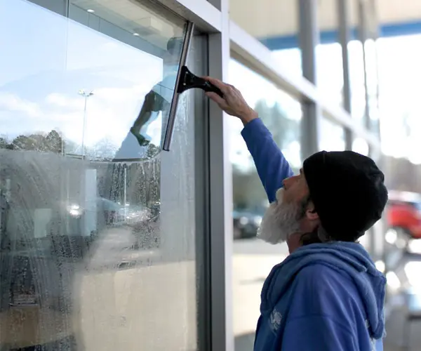 man in a blue sweatshirt and black hat wiping a window clean